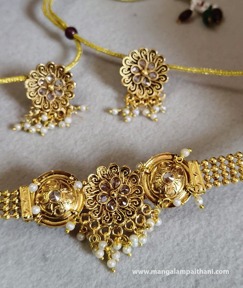A gold-plated choker necklace with multicolored floral patterns and a pair of matching earrings.