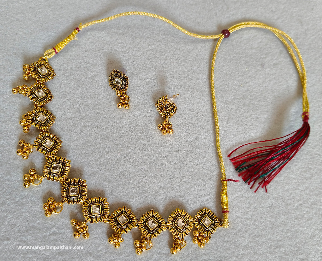 A gold-plated choker necklace set with a pair of earrings, featuring kundan-style embellishments and a red tassel hanging from the necklace
