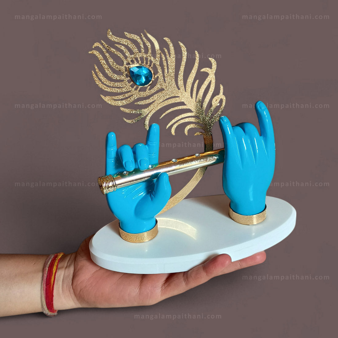 Decorative idol with blue hands holding a golden flute and a feather with a blue gem on a white base.
